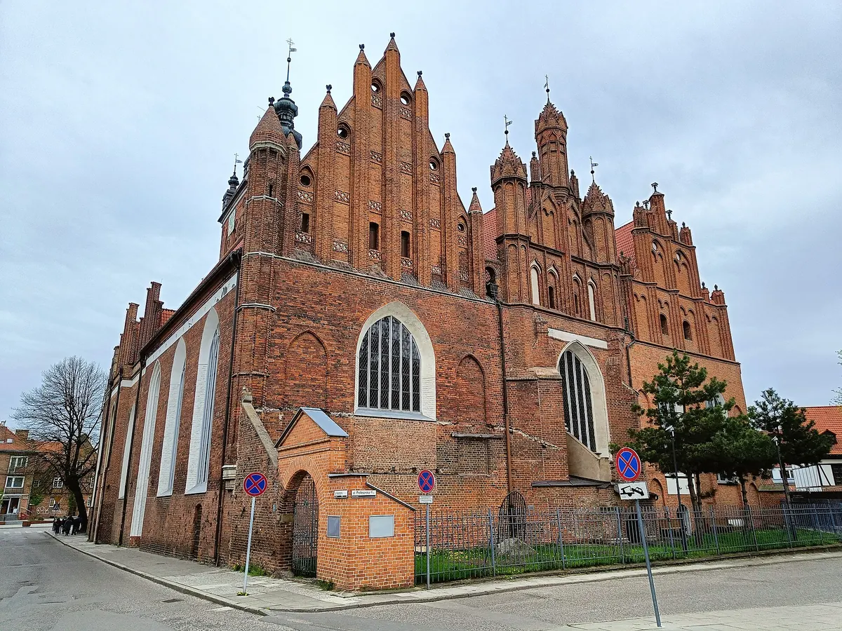 Červenocihlový východní závěr kostela sv. Kateřiny v Gdaňsku pod bledou oblohou, se stupňovitými štíty, fiálami a věží s měděnou střechou v pozadí